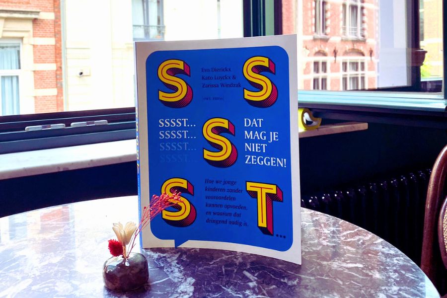 Het boek 'Sssst... Dat mag je niet zeggen.' staat op een tafel. De cover is blauw, met grote gele letters. 